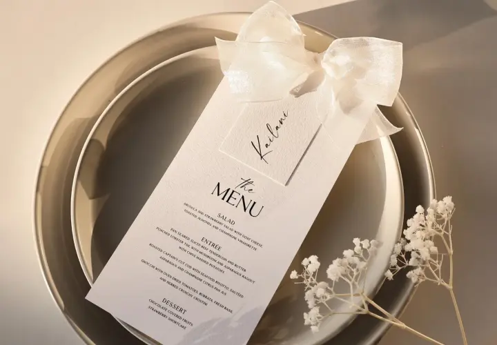Menu de mariage élégant sur une assiette, orné d'un ruban et de petites fleurs blanches.