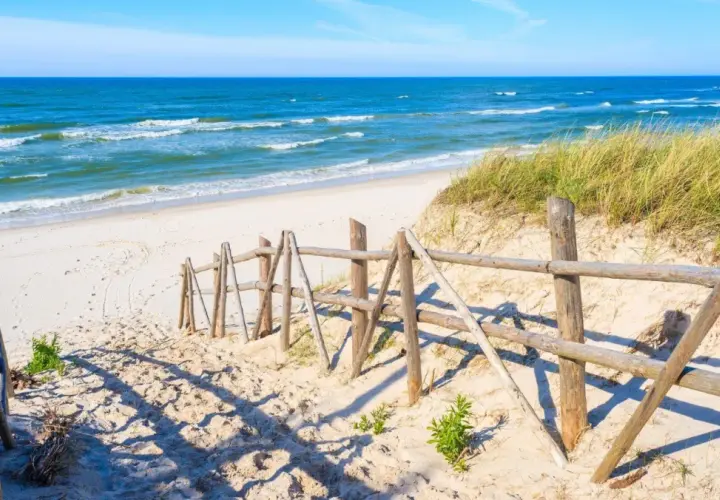 Piękna plaża w Łebie, idealne miejsce na spacer. Drewniane płotki prowadzą do morza, a trawy na wydmach dodają uroku.