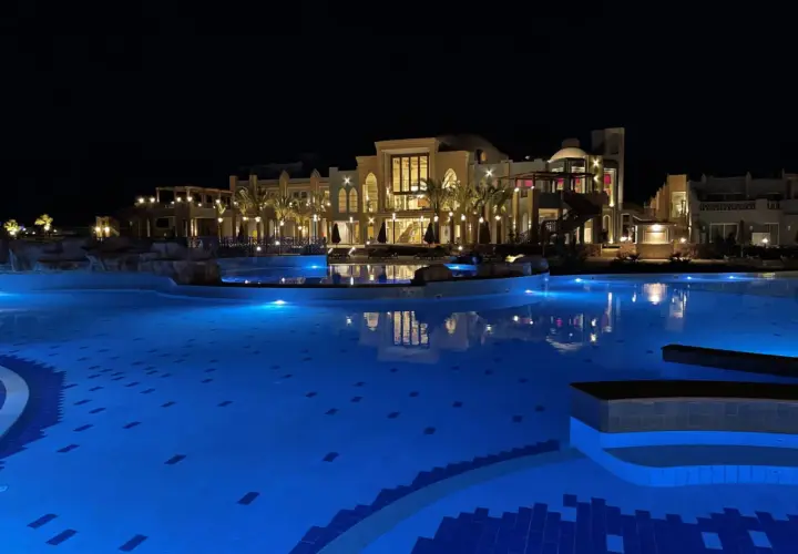 Nocny basen z niebieskim podświetleniem i luksusowym budynkiem hotelu Lazuli Marsa Alam w tle.