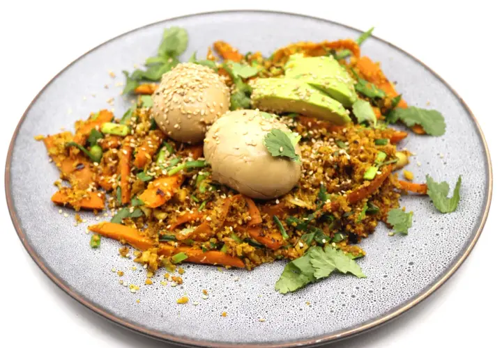 Assiette de riz aux légumes et deux oeufs marinés japonais, parsemée de graines de sésame et de coriandre fraîche.