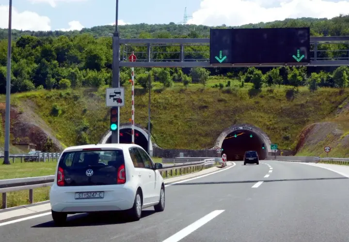 Biały samochód zbliża się do tunelu w Chorwacji. Znak drogowy informuje o opłatach za autostrady.