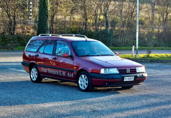 Ciemnoczerwony Fiat Tempra S.W. 4x4 z relingami dachowymi zaparkowany na tle drzew.