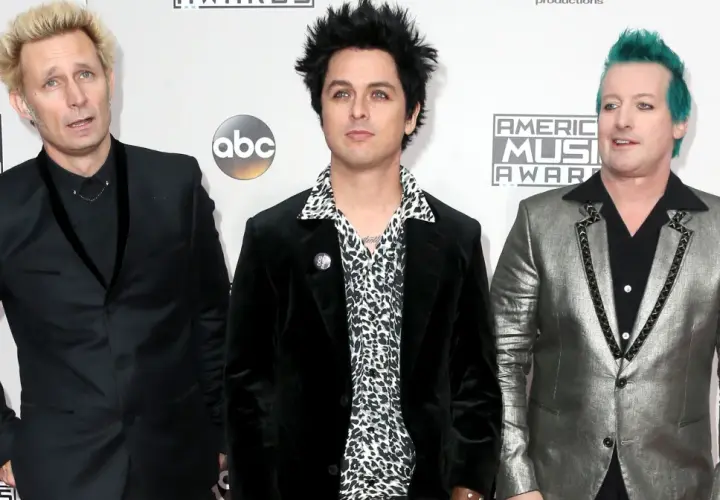 Trzech członków Green Day: Billie Joe Armstrong, Mike Dirnt i Tré Cool, pozują na czerwonym dywanie.
