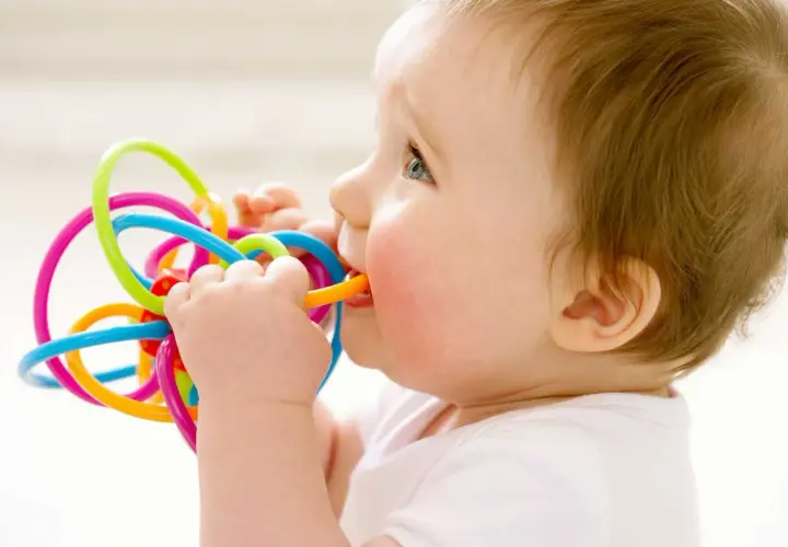 Bambino di 1 anno con dolore ai denti, che morde un giocattolo colorato per alleviare il fastidio.