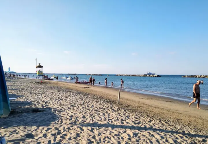 Plage animée à Gatteo Mare, avec des baigneurs, des enfants jouant dans l'eau et un poste de secours. Un bateau navigue au loin.