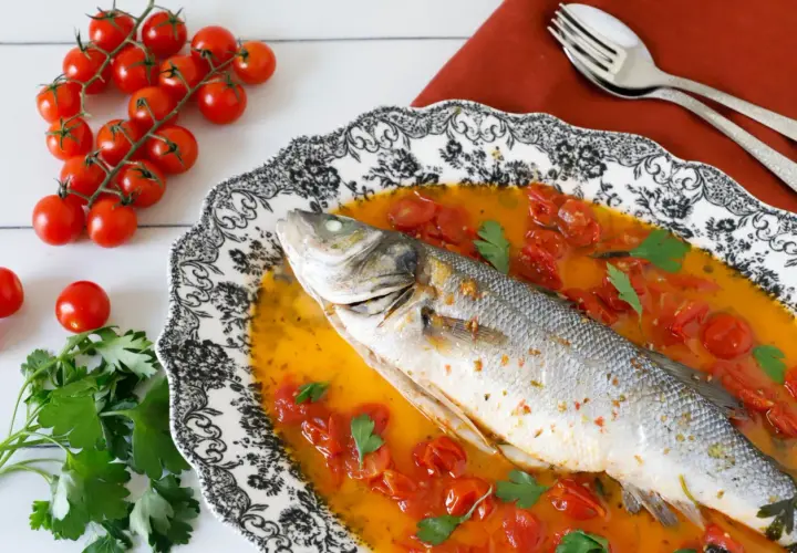 Spigola all'acqua pazza, un piatto succulento con pomodorini e prezzemolo, pronto per essere gustato.