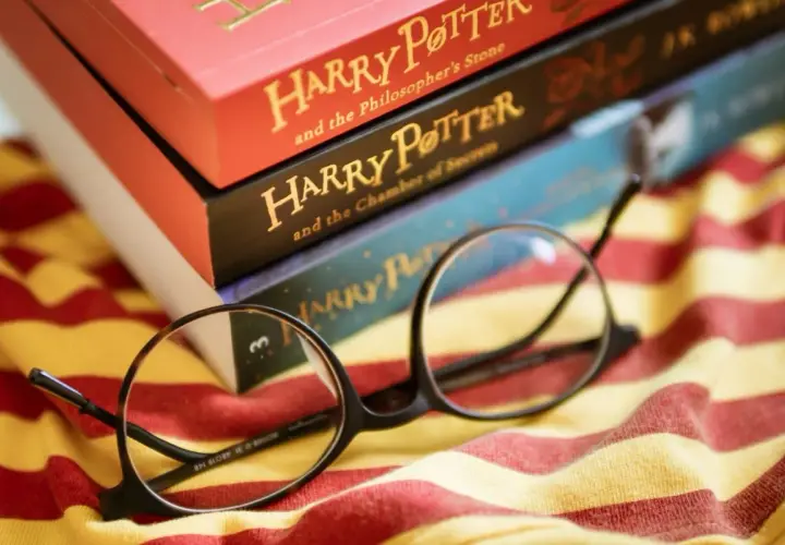 Okulary Harry'ego Pottera leżą na tle książek z serii i szalika Gryffindoru. To idealny cytat z Harrego Pottera dla każdego fana.
