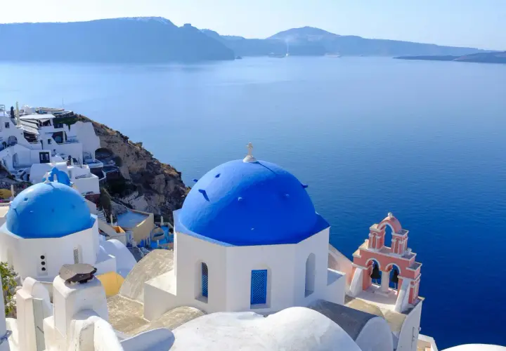 Białe domy i niebieskie kopuły kościołów na Santorini, idealne miejsce na wakacje. Dowiedz się, jak dolecieć na Santorini.