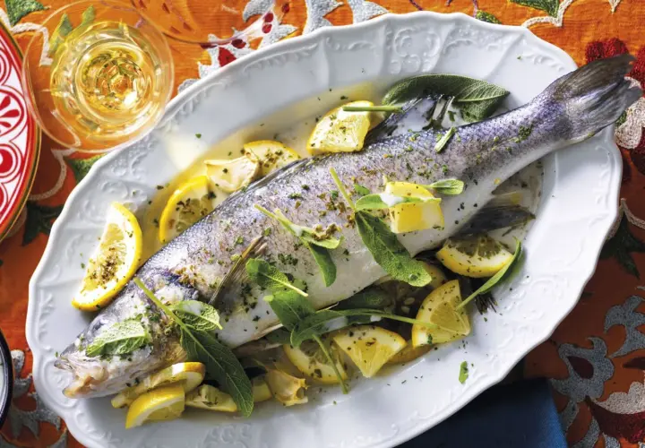 Un succulento branzino in padella, guarnito con spicchi di limone e foglie di salvia, pronto per essere gustato.