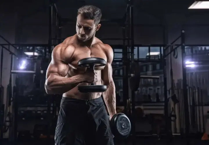 Mężczyzna ćwiczy biceps z hantlami. Ile serii na biceps w tygodniu? To pytanie zadaje sobie wielu trenujących.
