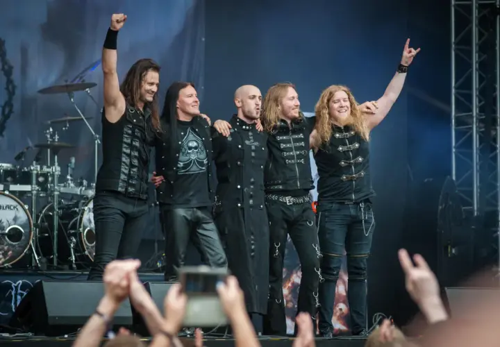 Zespół Beast in Black na koncercie, pięciu muzyków w czarnych strojach pozuje na scenie.