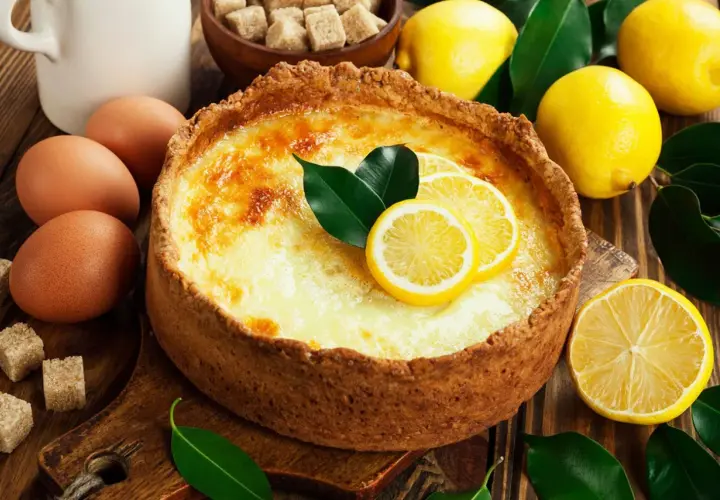 Un délicieux flan au citron, garni de rondelles de citron et de feuilles vertes, entouré de citrons frais, d'œufs et de sucre.