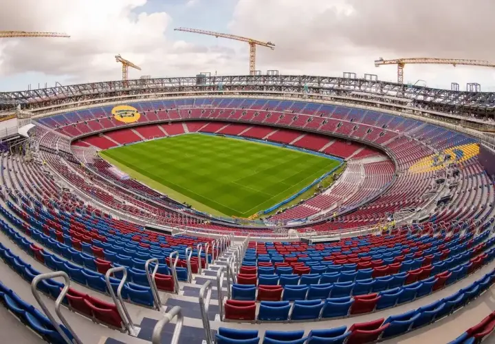 Widok na budowane nowe Camp Nou. Krzesełka w kolorach czerwonym i niebieskim czekają na kibiców, a nad stadionem górują dźwigi.