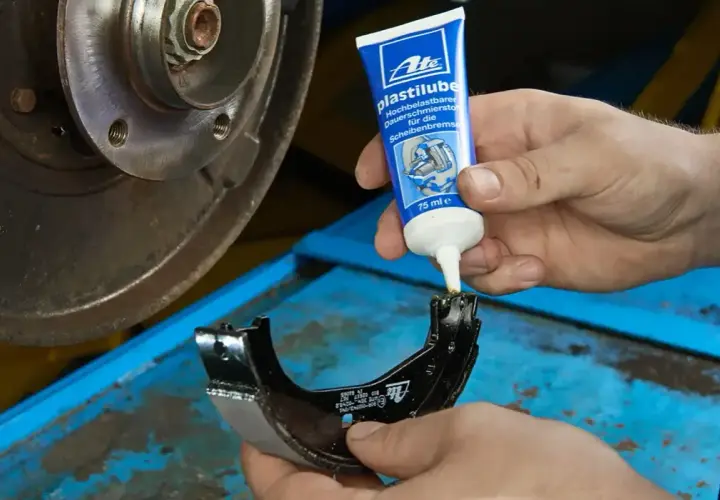 Mechanik aplikuje smar ceramiczny do hamulców na szczękę hamulcową, przygotowując ją do montażu.