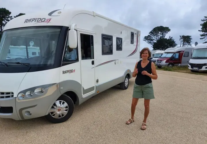 Une femme pose devant son camping-car Rapido, sur une aire de camping-car près de la Côte de Granit Rose.