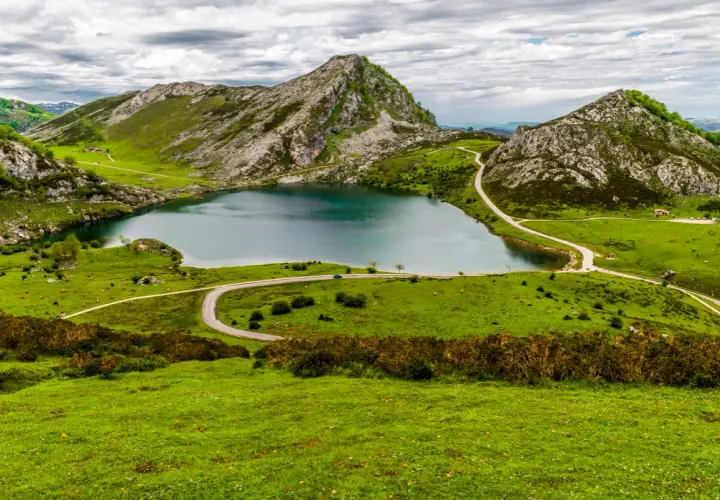 Lago en Picos de Europa que ver: paisaje verde con montañas rocosas, un lago azul y carreteras sinuosas.