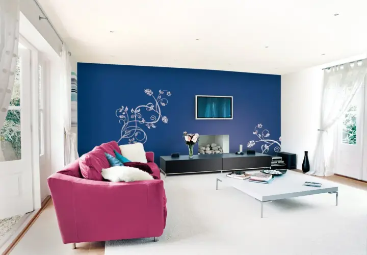 Un salone moderno con divano fucsia e parete blu con decorazioni floreali. Idee per come pitturare un salone con stile.