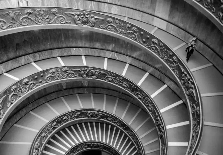 Un escalier en colimaçon orné, rappelant une coupole du Vatican, avec une personne solitaire descendant ses marches.