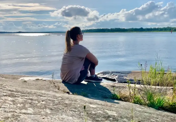 Kvinna sitter på en klippa vid havet, njuter av lugnet. Perfekt för mental avslappning och att ladda batterierna för att sova gott.