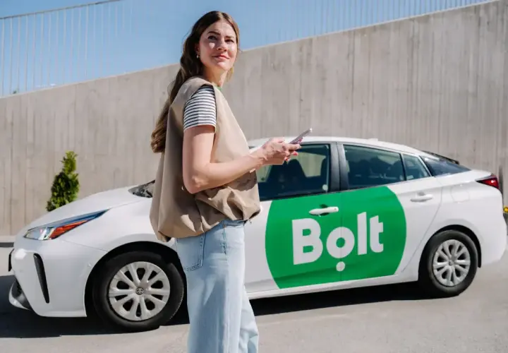 Kobieta z telefonem stoi obok białego samochodu Bolt z zielonym logo.