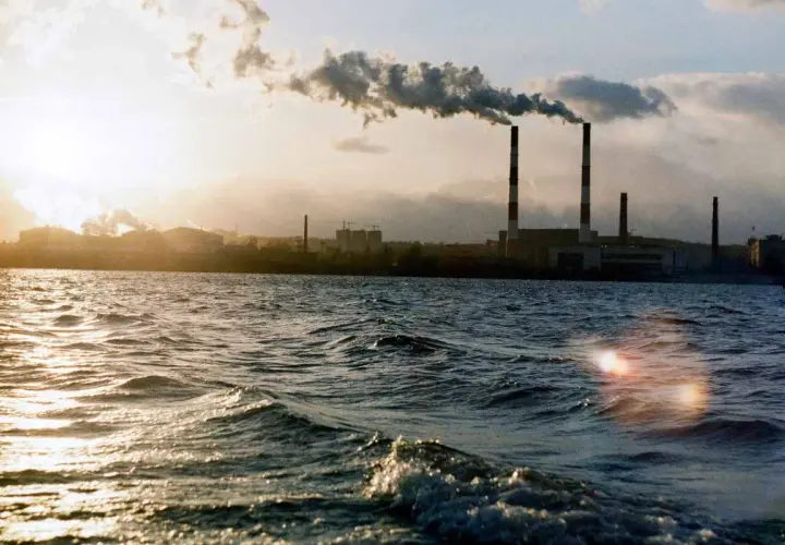 Chimeneas industriales emiten humo sobre un río, un ejemplo de cómo se mide la calidad del aire.