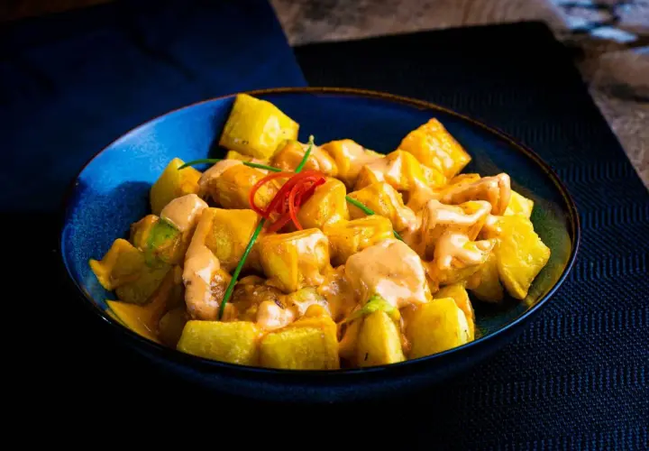 Patatas bravas receta: trozos dorados de patata cubiertos con una cremosa salsa rosada y decorados con pimiento rojo y cebolleta.