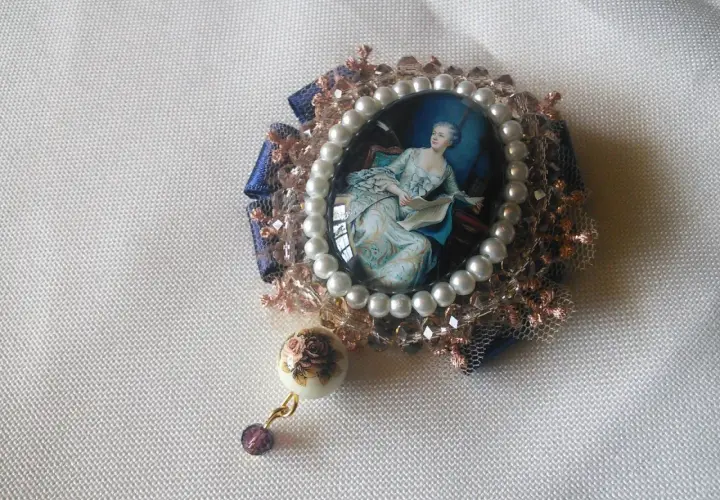 Broche con camafeos, perlas y detalles florales. Una dama elegante lee un libro en un retrato ovalado, rodeada de encaje y cristales.