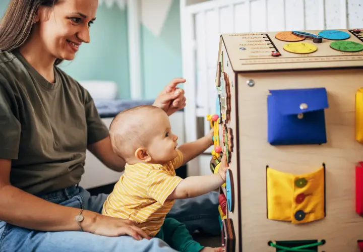Maluch z radością odkrywa tablicę manipulacyjną. Od jakiego wieku taka zabawka? Od momentu, gdy dziecko zaczyna siedzieć i chwytać.