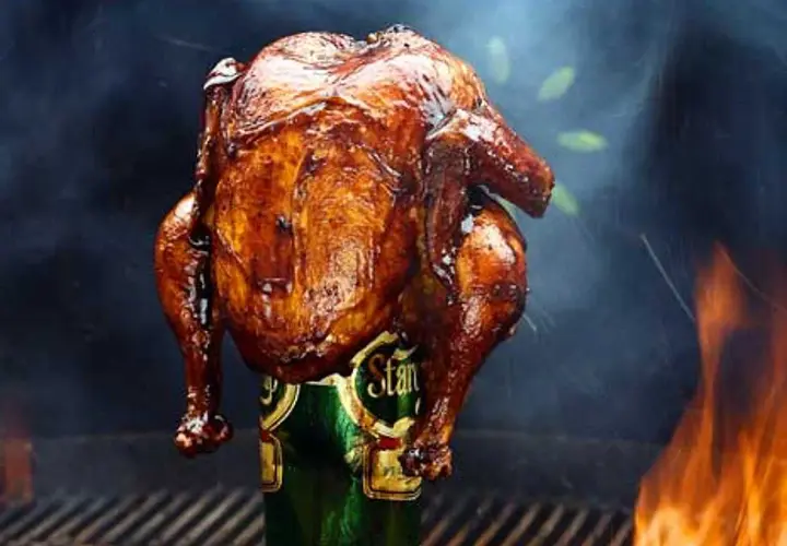 En saftig, gyllene hel kyckling tillagas stående på en ölburk, omgiven av rök och flammor. En klassisk beer can chicken.