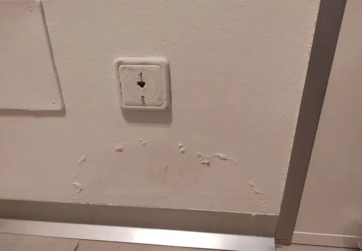 Purchle na ścianie od wilgoci, widoczne obok gniazdka elektrycznego i panelu.