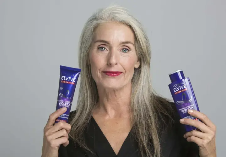 Mujer con cabello gris muestra productos Elvive Color-Vive, ideales como remedios caseros para quitar el amarillo del pelo y matizar.