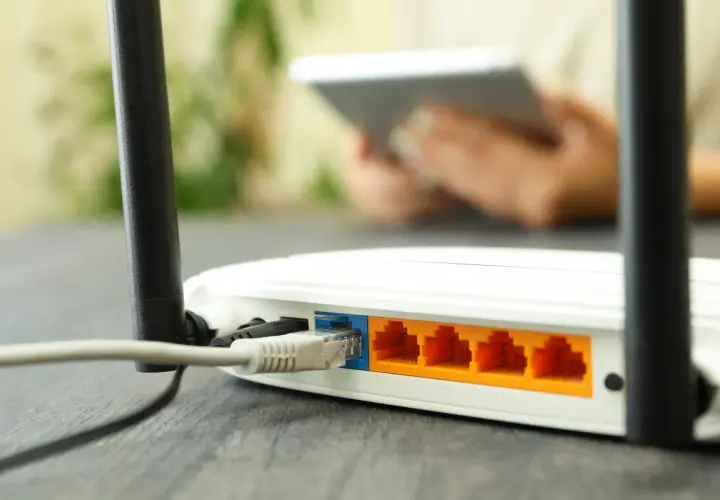 Router z podłączonym kablem Ethernet i portami LAN. W tle osoba z tabletem.