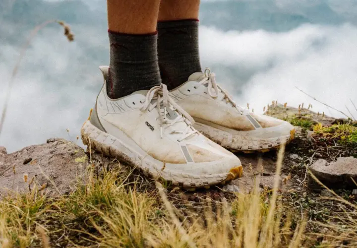 A pair of well-worn, white norda 001a trail running shoes stand on a rocky, grassy peak, ready for adventure.