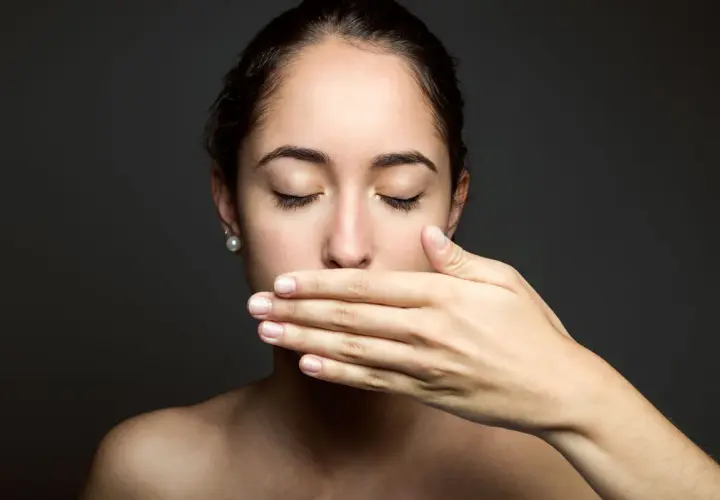 Donna con mano sulla bocca, occhi chiusi, come se avesse scoperto che il filo interdentale puzza.