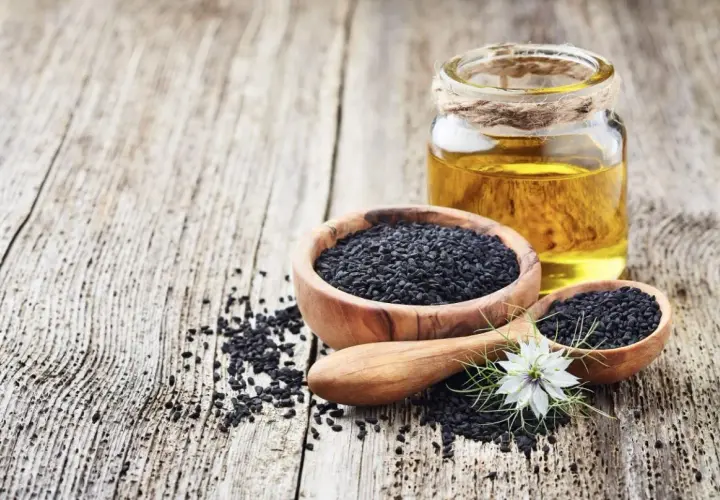 Semi neri in ciotole di legno e un flacone di olio di nigella, con un fiore bianco.