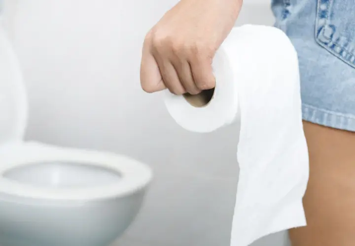 Dłoń trzymająca rolkę papieru toaletowego, w tle sedes. Stres wywołuje biegunka.