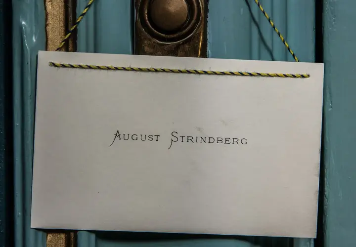 En skylt med texten "August Strindberg" hänger på en blå dörr, kanske vid Strindbergsmuseet.
