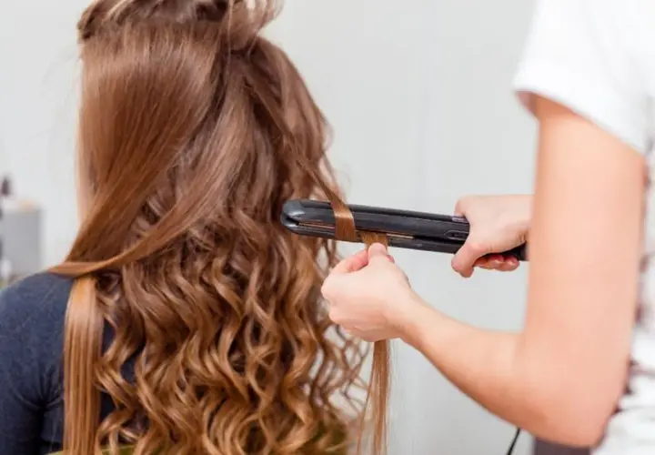 Creando ondas al agua con una plancha. El cabello castaño de una chica se riza, transformándose en suaves ondas.