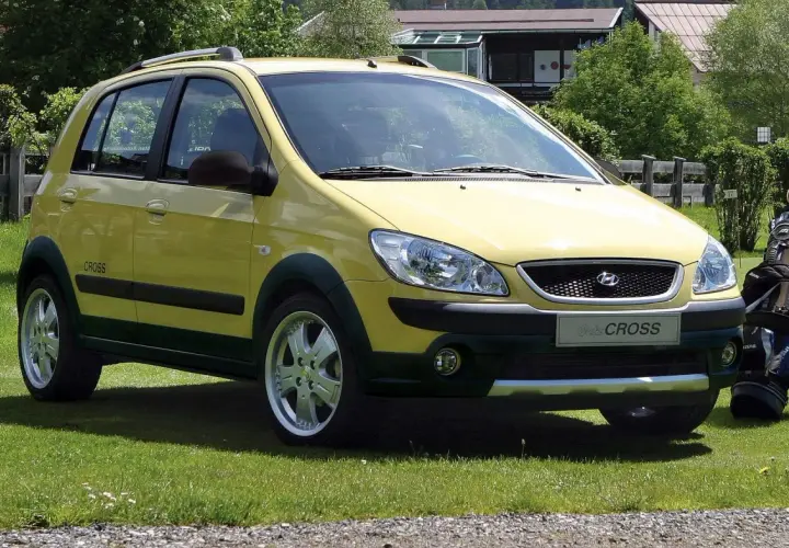 Żółty Hyundai Getz Cross zaparkowany na trawie obok torby golfowej.