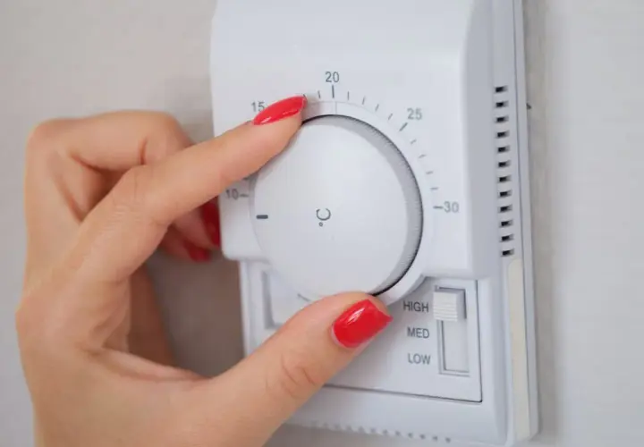 Mano ajustando el termostato para la temperatura calefacción noche. Se ve el dial con grados y el selector de potencia.
