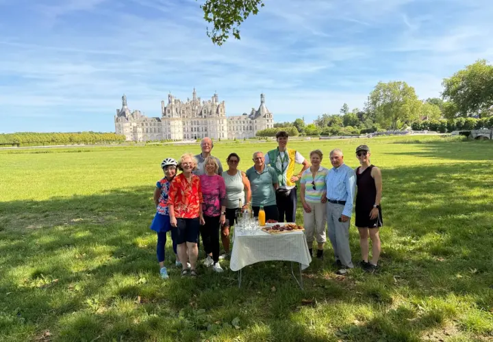 A group enjoys a picnic during their Loire Valley cycling tours, with the magnificent Château de Chambord in the background.