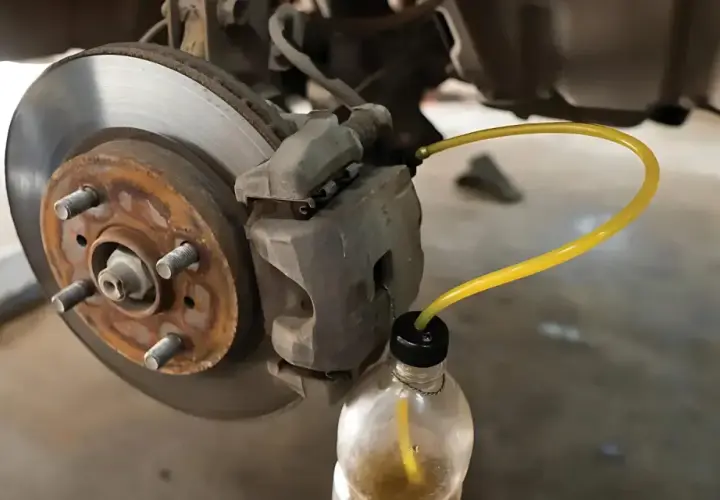 Bleeding car brakes with the cap off the bleed screw, using a yellow tube to drain fluid into a bottle.