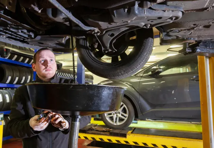 Mechanik spuszcza zużyty olej z samochodu. Dowiedz się, ile kosztuje wymiana oleju w warsztacie.