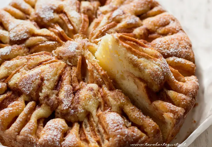 Una deliziosa torta di mele, cosparsa di zucchero a velo, con una fetta sollevata che mostra la morbida consistenza.