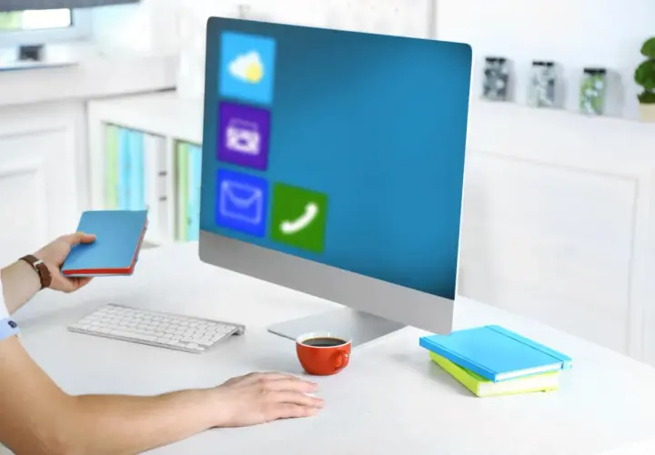 Pracownik biurowy z notatnikiem w dłoni, przed monitorem z ikonami aplikacji, jak w WPS Office.