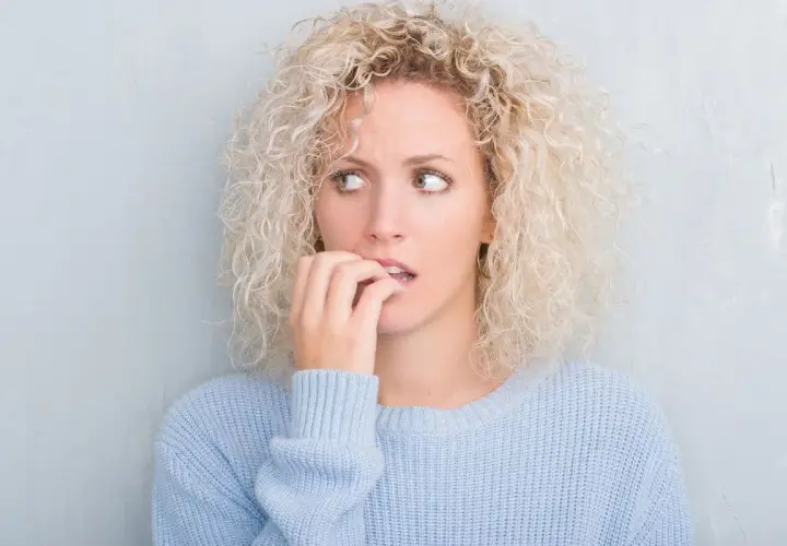 Ragazza con capelli ricci biondi, maglione azzurro, morde le unghie, con brividi di freddo e ansia.