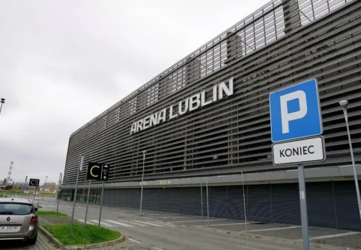 Nowoczesny stadion Arena Lublin z napisem na fasadzie. Obok znak parkingu i drogowskazy.