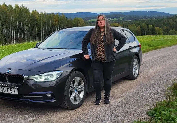 Kvinna vid en svart BMW kombi i svensk landsbygd. Kanske ett bmw b47 problem som gör att hon stannat här.