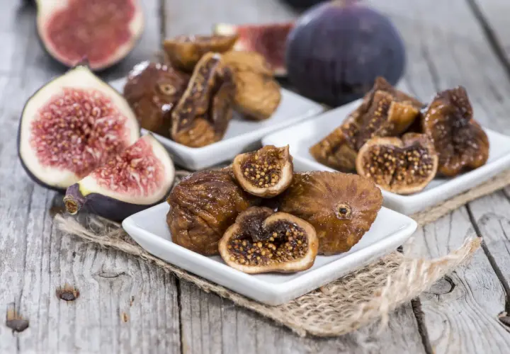 Des figues fraîches et des figues séchées au four sur des assiettes blanches, posées sur du bois rustique.
