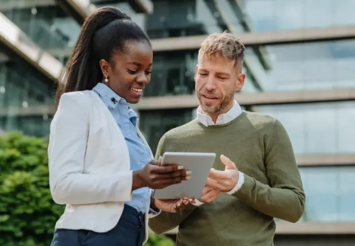Two professionals discuss their MPA online program on a tablet outside a modern building.